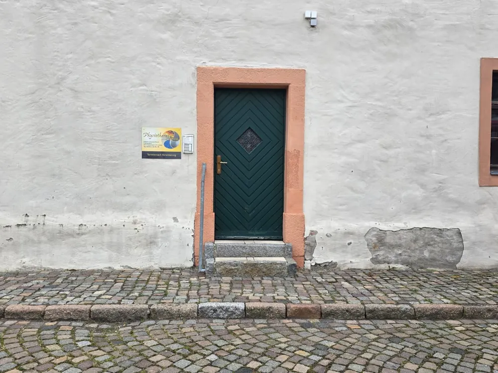Eingang der Praxis in der Victoriastraße 9: grüne Holztür mit zwei Stufen und Handlauf links, das Praxisschild daneben